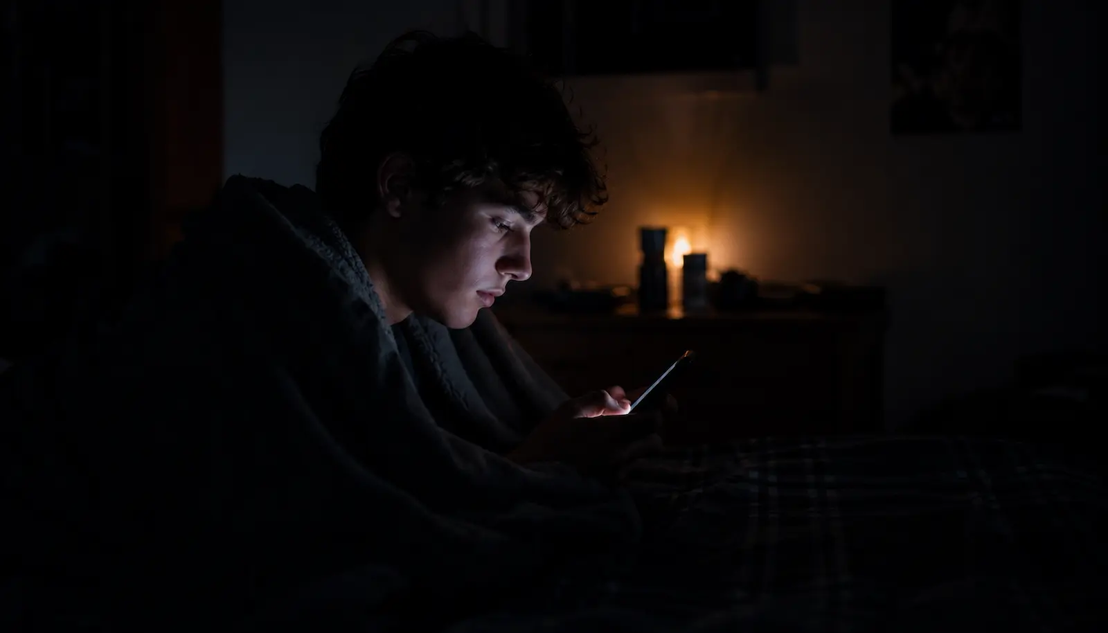Jugendlicher nachts im dunklen Zimmer im Schein des Smartphones – Schlafmangel und Social Media bei Jugendlichen
